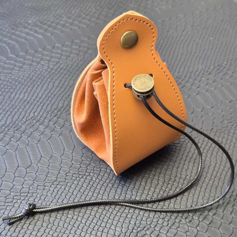 A brown leather dice bag with buttons and rope to tightly close it. Displayed on a black textured background