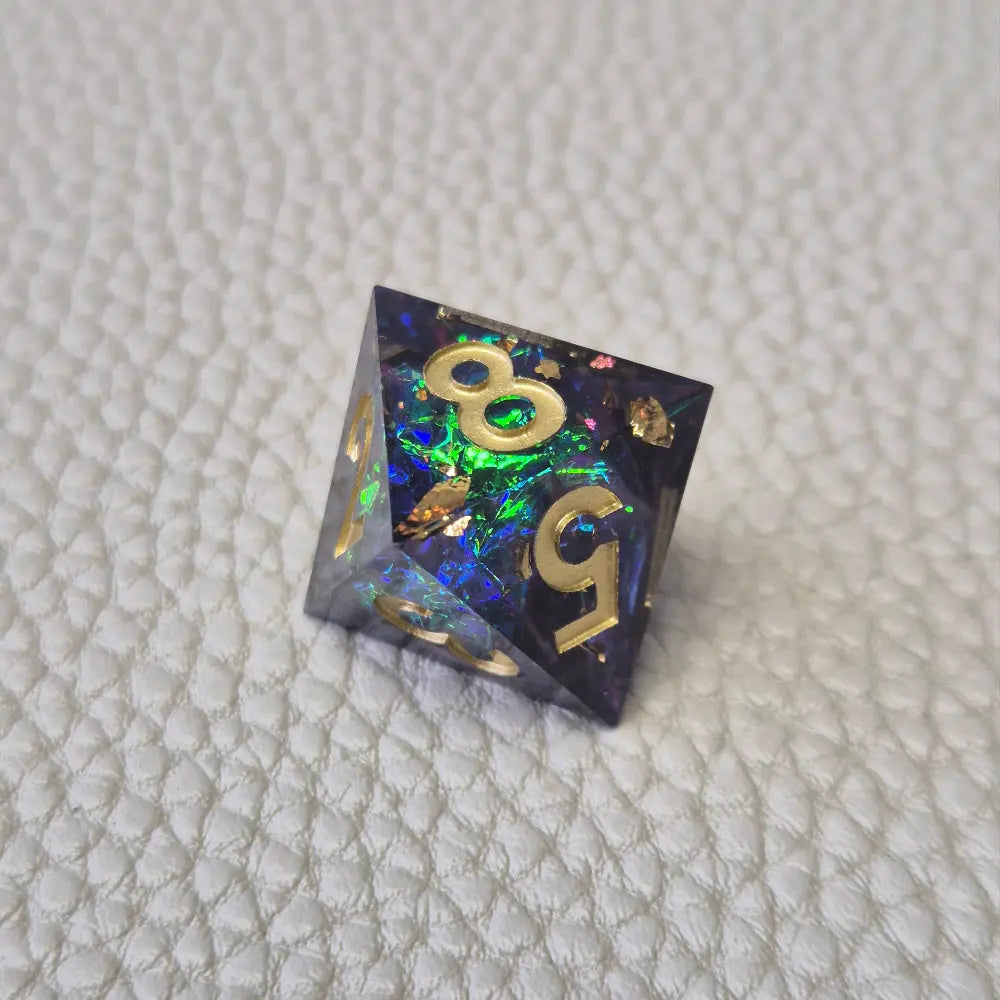 A set of blue sharp edge resin dice with green confetti inside on a white textured surface