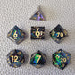 A set of blue sharp edge resin dice with green confetti inside on a white textured surface