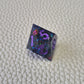 A set of purple sharp edge resin dice with blue confetti inside on a white textured surface