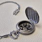 A silver coloured full metal pocket watch themed dice locket, with engraved backside and detailed dragon on the front. Contains full set of metal dice inside