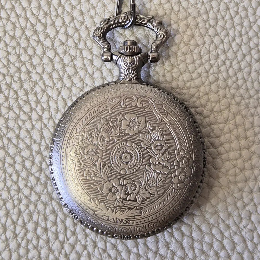 A silver coloured full metal pocket watch themed dice locket, with engraved backside and detailed dragon on the front. Contains full set of metal dice inside