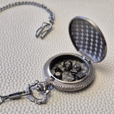 A silver coloured full metal pocket watch themed dice locket, with engraved backside and detailed kraken on the front. Contains full set of metal dice inside