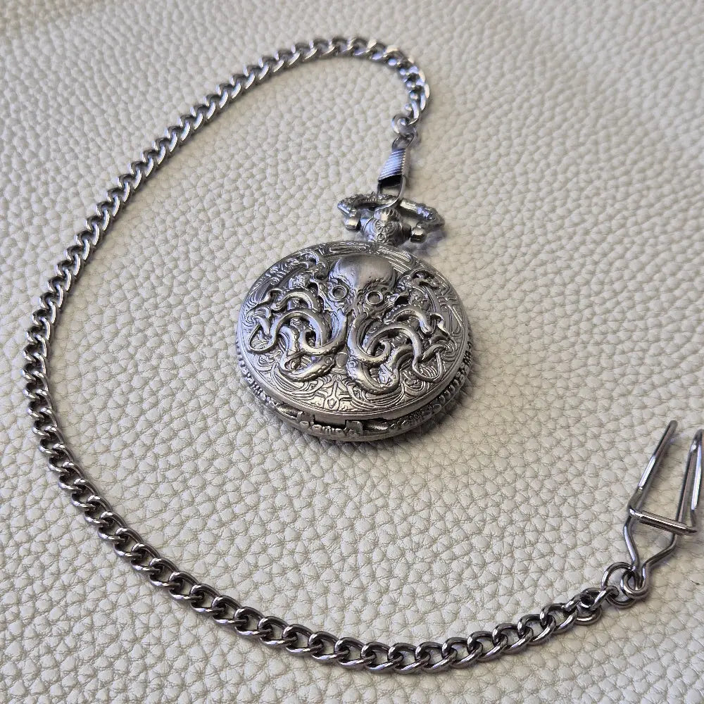 A silver coloured full metal pocket watch themed dice locket, with engraved backside and detailed kraken on the front. Contains full set of metal dice inside