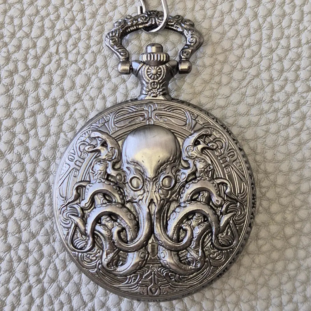 A silver coloured full metal pocket watch themed dice locket, with engraved backside and detailed kraken on the front. Contains full set of metal dice inside