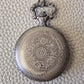 A silver coloured full metal pocket watch themed dice locket, with engraved backside and detailed kraken on the front. Contains full set of metal dice inside