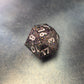 A set of black sharp edge resin dice with white numbers and colourfull sparkles on a blue metal surface