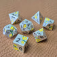 Metal D&D dice set with matte silver finish and painted yellow flowers, displayed on textured leather background.