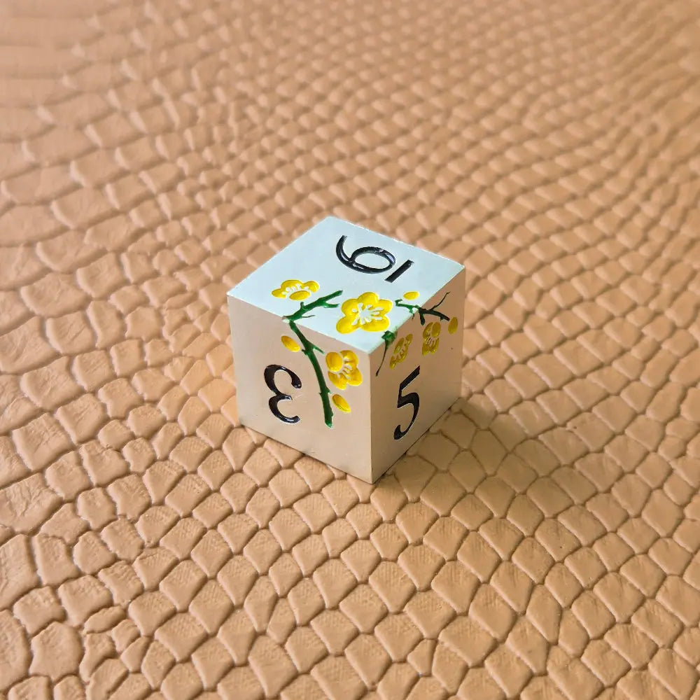 Metal D&D dice set with matte silver finish and painted yellow flowers, displayed on textured leather background.