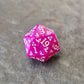 Purple acrylic D20 with white ornate numbering, styled with arcane fantasy motifs, displayed on a stone surface.