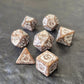 Brown khaki acrylic dice set with white ornate numbers, arranged on a textured grey stone background.