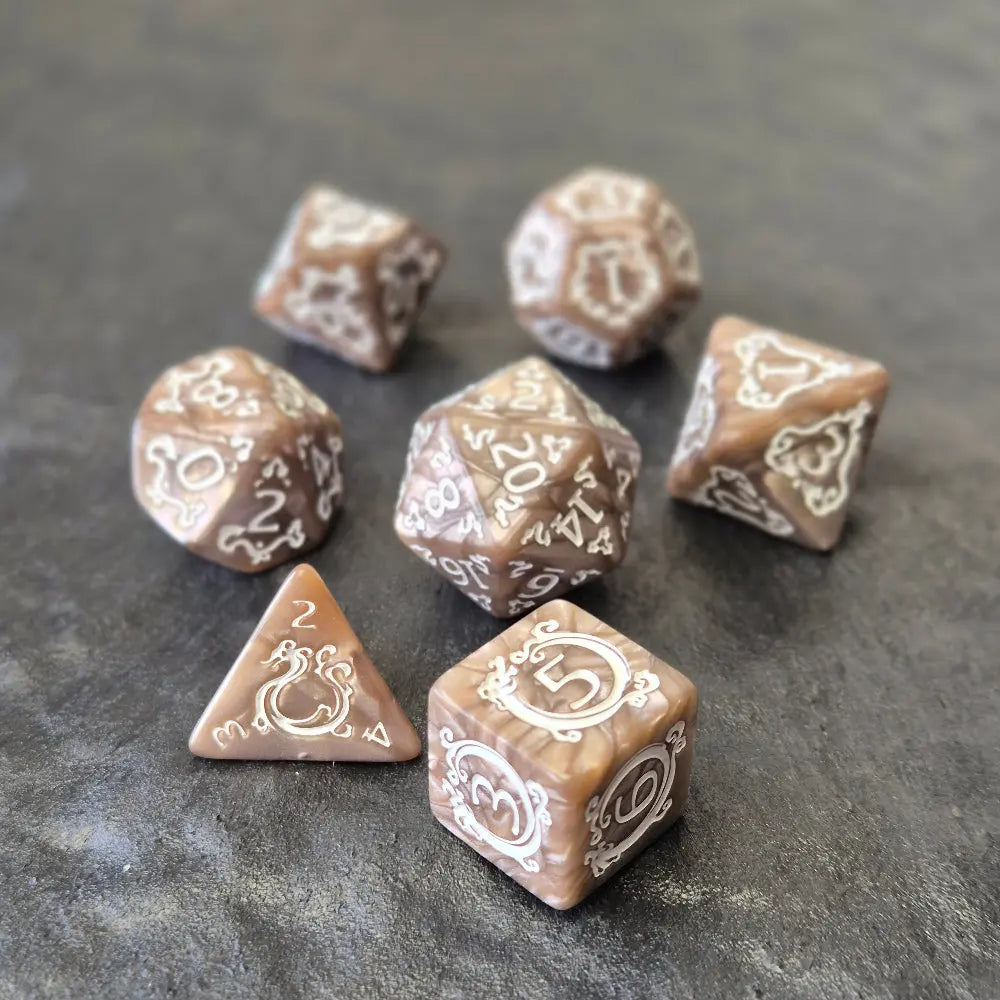 Brown khaki acrylic dice set with white ornate numbers, arranged on a textured grey stone background.