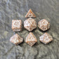 Brown khaki acrylic dice set with white ornate numbers, arranged on a textured grey stone background.
