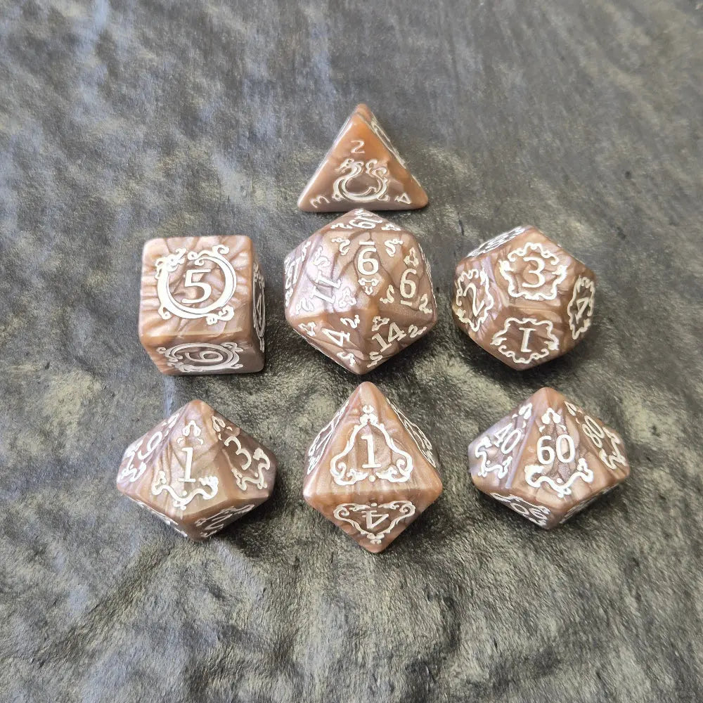 Brown khaki acrylic dice set with white ornate numbers, arranged on a textured grey stone background.