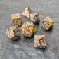 Gold acrylic polyhedral dice set with ornate white fantasy-style numbers displayed on a stone surface, featuring a close-up of a d20.
