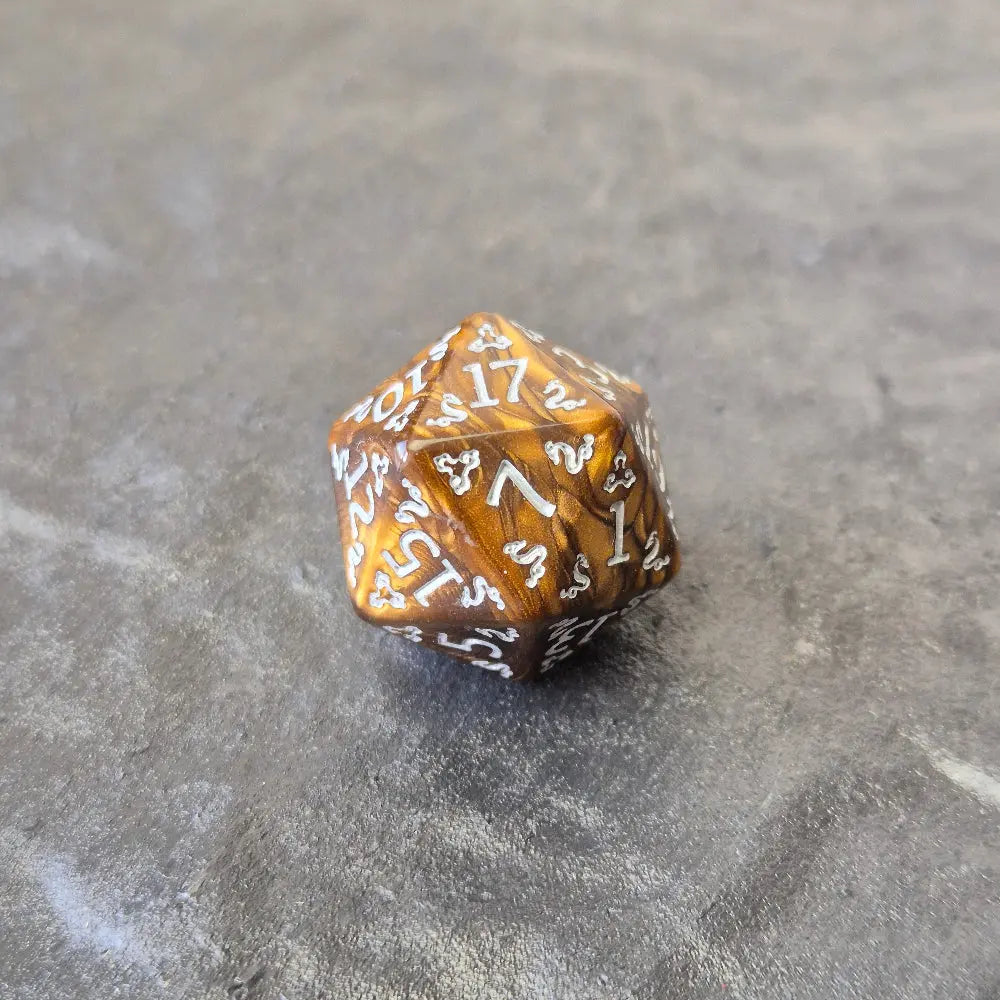 Gold acrylic D20 with ornate white fantasy-style numbers displayed on a stone surface, featuring a close-up of a d20.