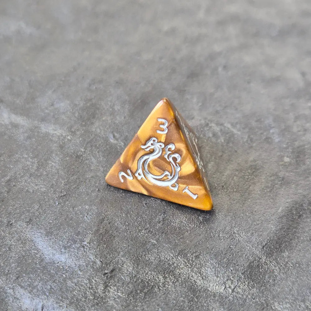 Gold acrylic D4 with ornate white fantasy-style numbers displayed on a stone surface, featuring a close-up of a d20.