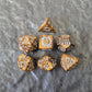 Gold acrylic polyhedral dice set with ornate white fantasy-style numbers displayed on a stone surface