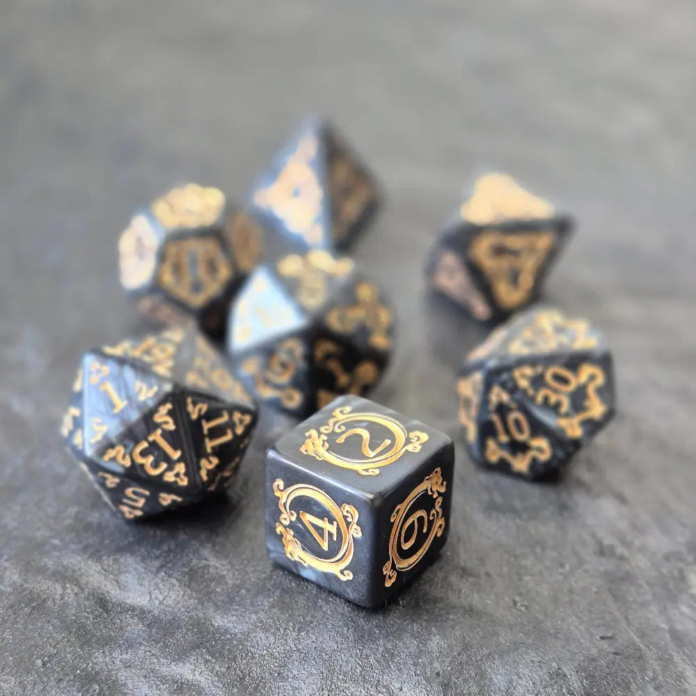 Acrylic D&D dice set with swirling black design and ornate golden numbering, displayed on a dark background.