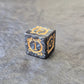 Acrylic D6 dice with swirling black design and ornate golden numbering, displayed on a dark background.