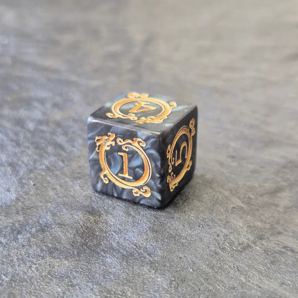 Acrylic D6 dice with swirling black design and ornate golden numbering, displayed on a dark background.