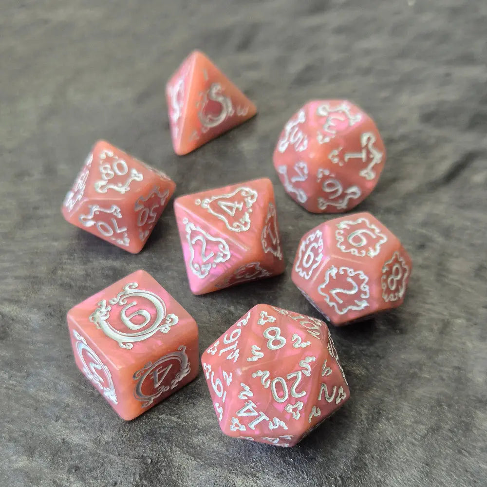 Pink acrylic D&D dice set with white arcane-style numbers and elegant swirls, displayed on a textured grey surface.