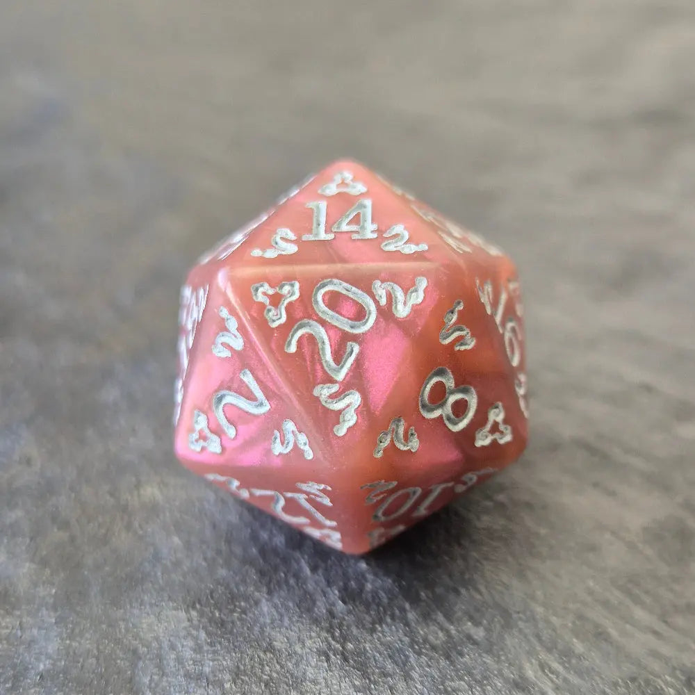 Pink acrylic D20 with white arcane-style numbers and elegant swirls, displayed on a textured grey surface.