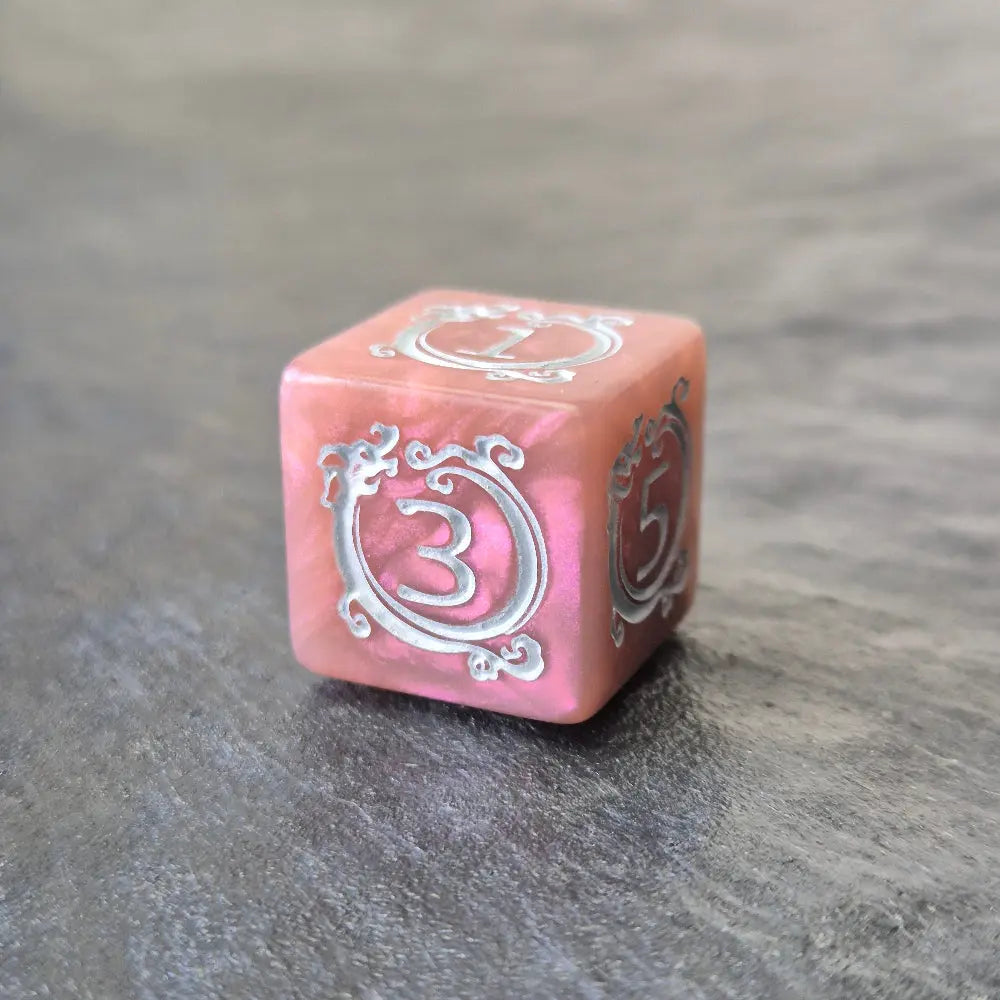 Pink acrylic D6 with white arcane-style numbers and elegant swirls, displayed on a textured grey surface.