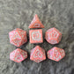 Pink acrylic D&D dice set with white arcane-style numbers and elegant swirls, displayed on a textured grey surface.