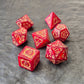 Red acrylic D&D dice set with golden arcane-style numbers and swirling patterns, displayed on a textured grey background.
