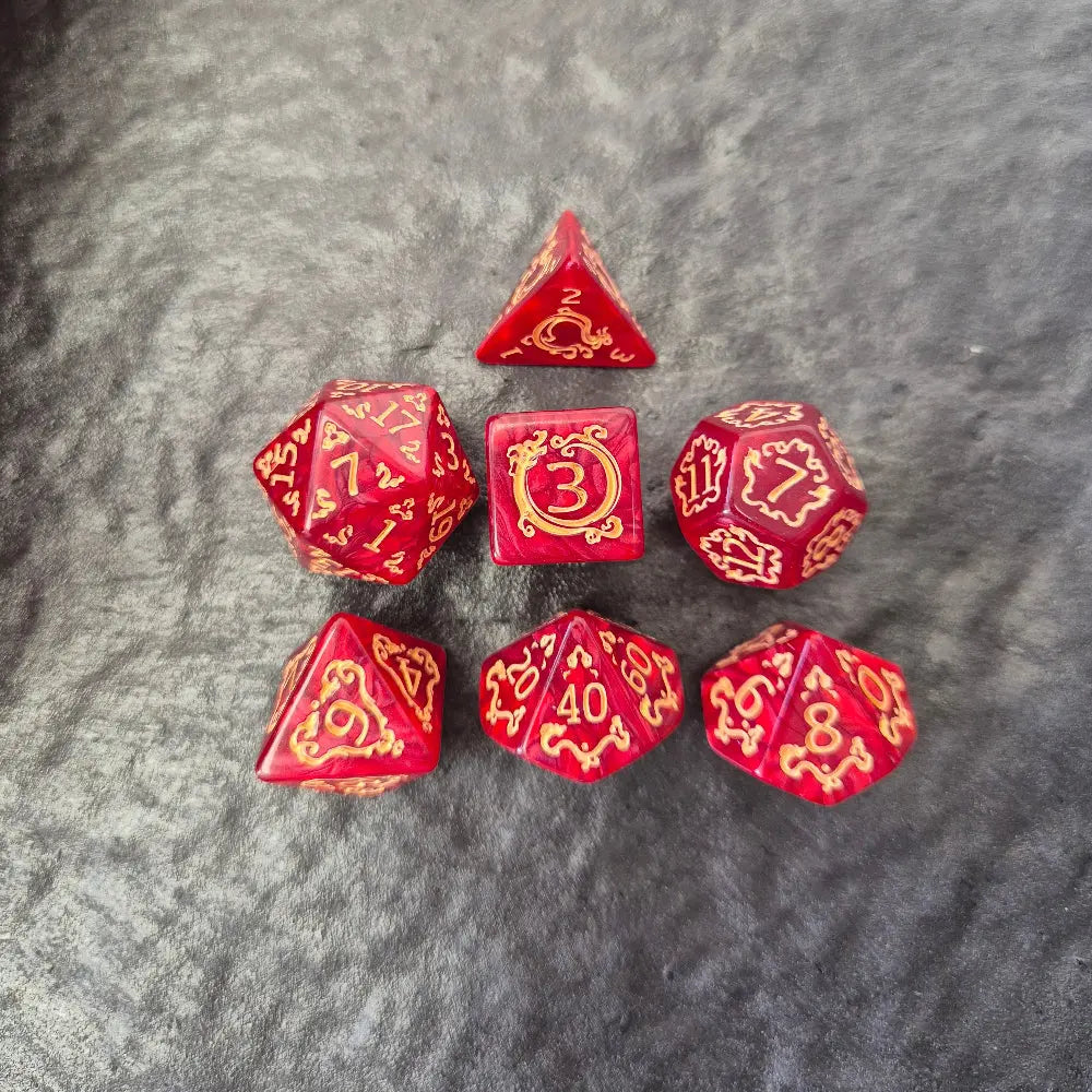 Red acrylic D&D dice set with golden arcane-style numbers and swirling patterns, displayed on a textured grey background.
