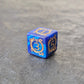 D6 blue acrylic dice with ornate gold numbering and arcane motifs, displayed on a dark stone surface.