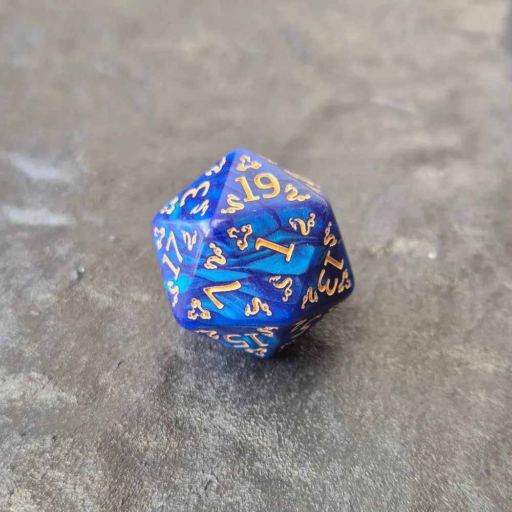 D20 blue acrylic dice with ornate gold numbering and arcane motifs, displayed on a dark stone surface.