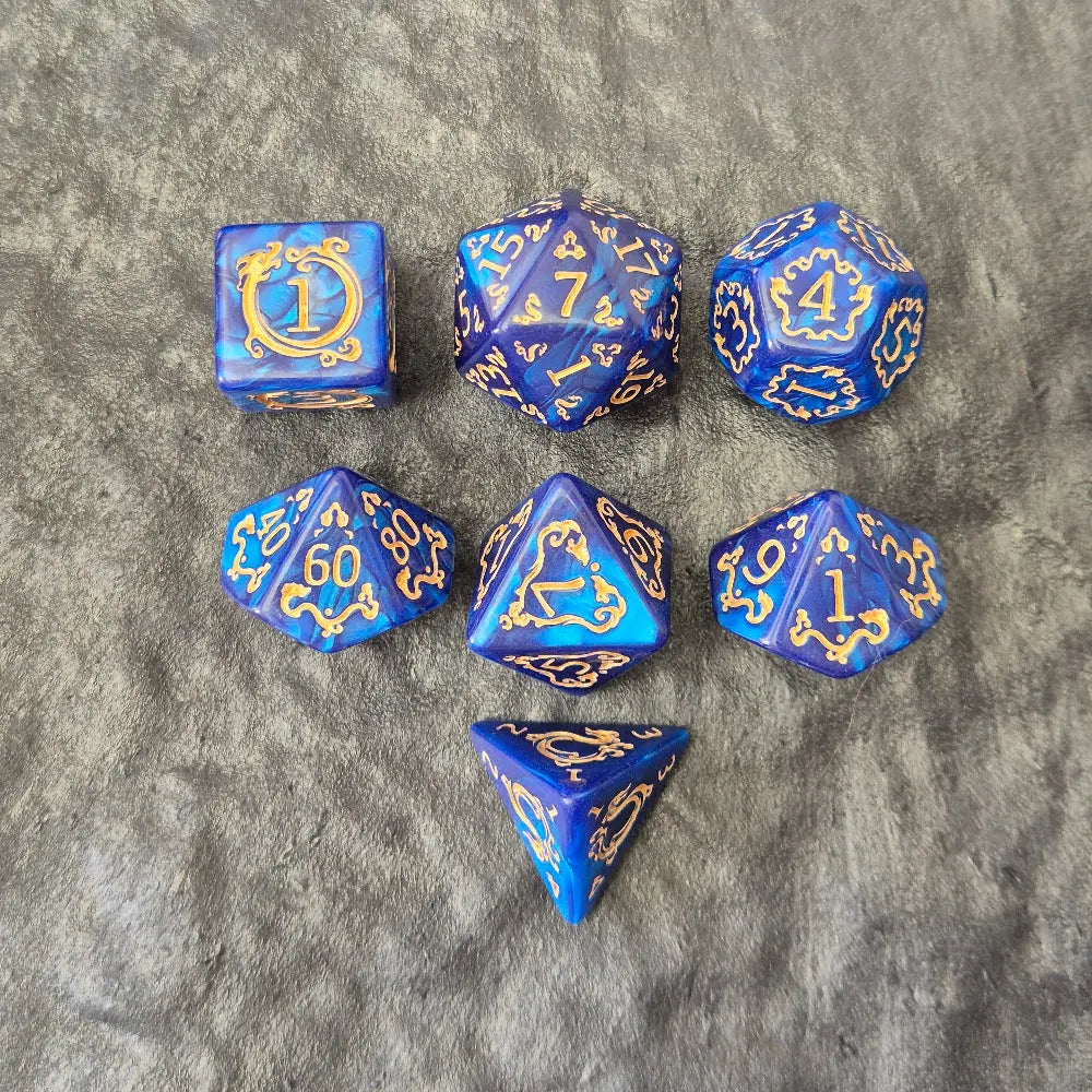 7-piece blue acrylic dice set with ornate gold numbering and arcane motifs, displayed on a dark stone surface.