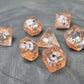 Orange resin polyhedral dice set with embedded cow miniatures and gold numbering, displayed on a textured grey background.