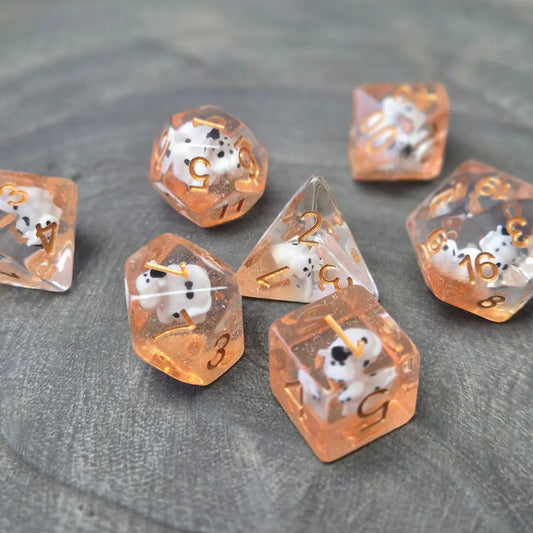 Orange resin polyhedral dice set with embedded cow miniatures and gold numbering, displayed on a textured grey background.