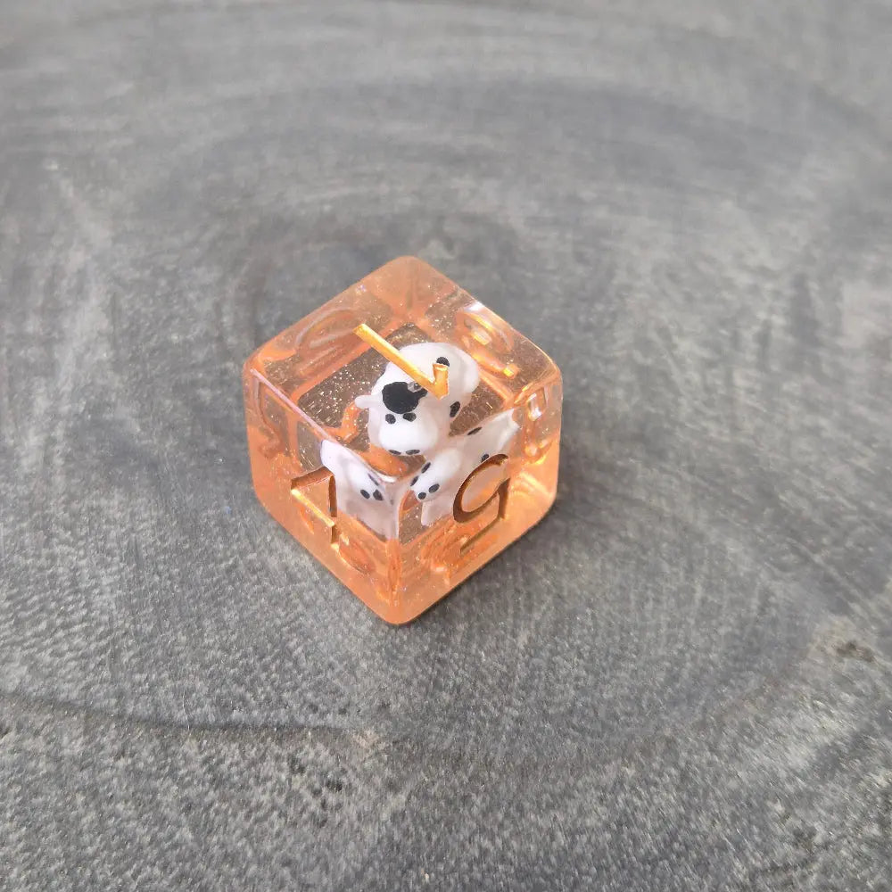 D6 Orange resin polyhedral dice with embedded cow miniatures and gold numbering, displayed on a textured grey background.