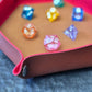 Foldable hexagon-shaped dice trays in red & brown shown open and filled with colorful polyhedral dice.