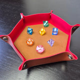 Foldable hexagon-shaped dice trays in red & brown shown open and filled with colorful polyhedral dice.