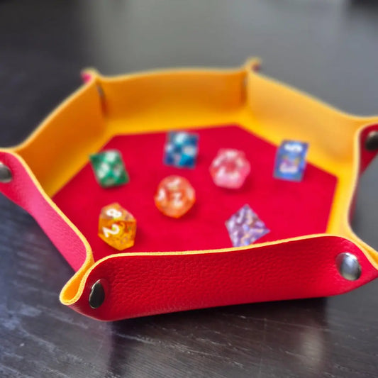 Foldable hexagon-shaped dice tray in yellow & red shown open and filled with colorful polyhedral dice.