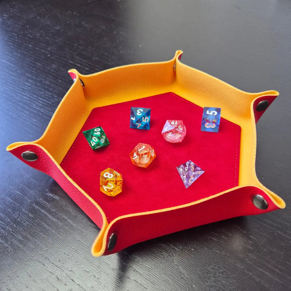Foldable hexagon-shaped dice tray in yellow & red shown open and filled with colorful polyhedral dice.