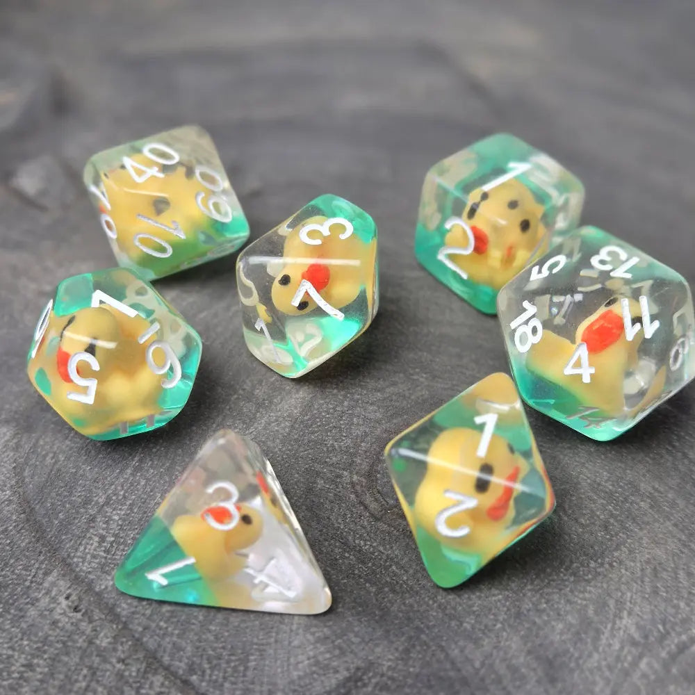 Close-up of transparent resin dice with tiny yellow ducks inside, placed on a textured stone surface.
