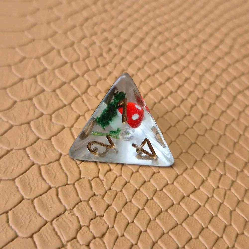 Clear resin D4 dice with red mushroom and moss encased inside, golden numbers, set on a textured leather background.