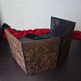 Foldable four-panel Dungeon Master screen with embossed fantasy scenes, displayed on a dark tabletop.